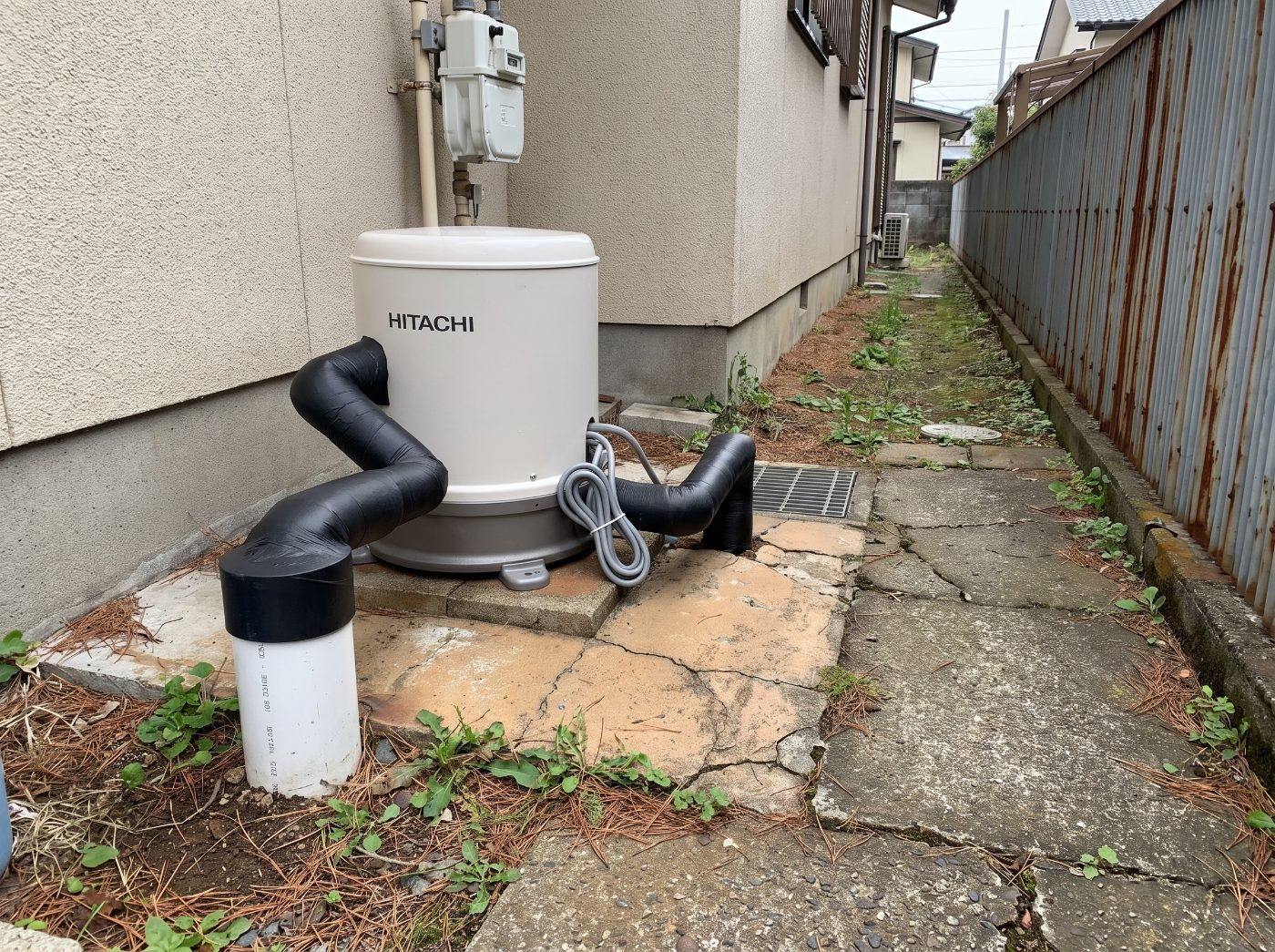 家屋脇に設置された井戸ポンプ（HITACHI浅井戸ポンプ）と地上に出たケーシングパイプ。井戸掘り完成事例